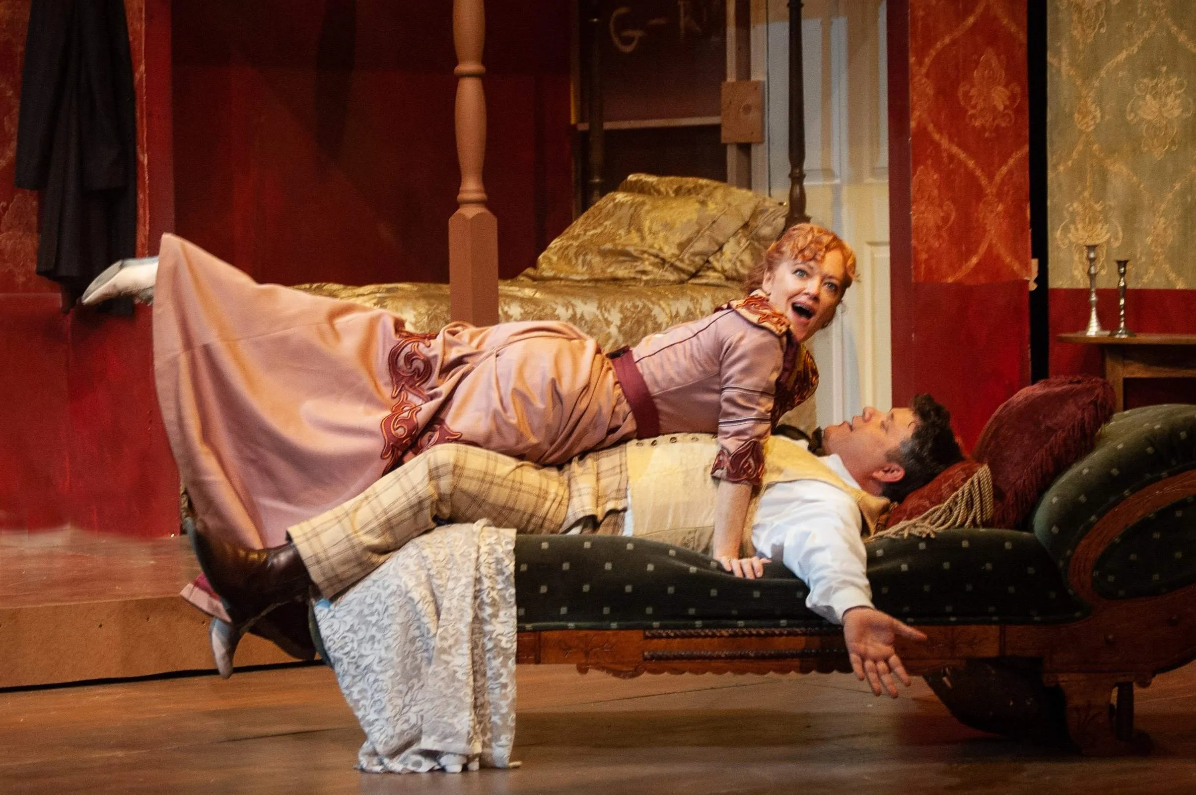 A man is laying down with a girl on his chest who is wearing a pink dress. The boy has a surprised look on his face.