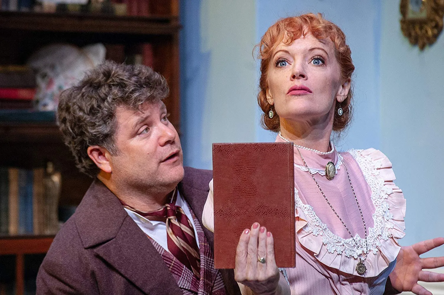 A woman in a pink shirt with a red book is watched by her husband.