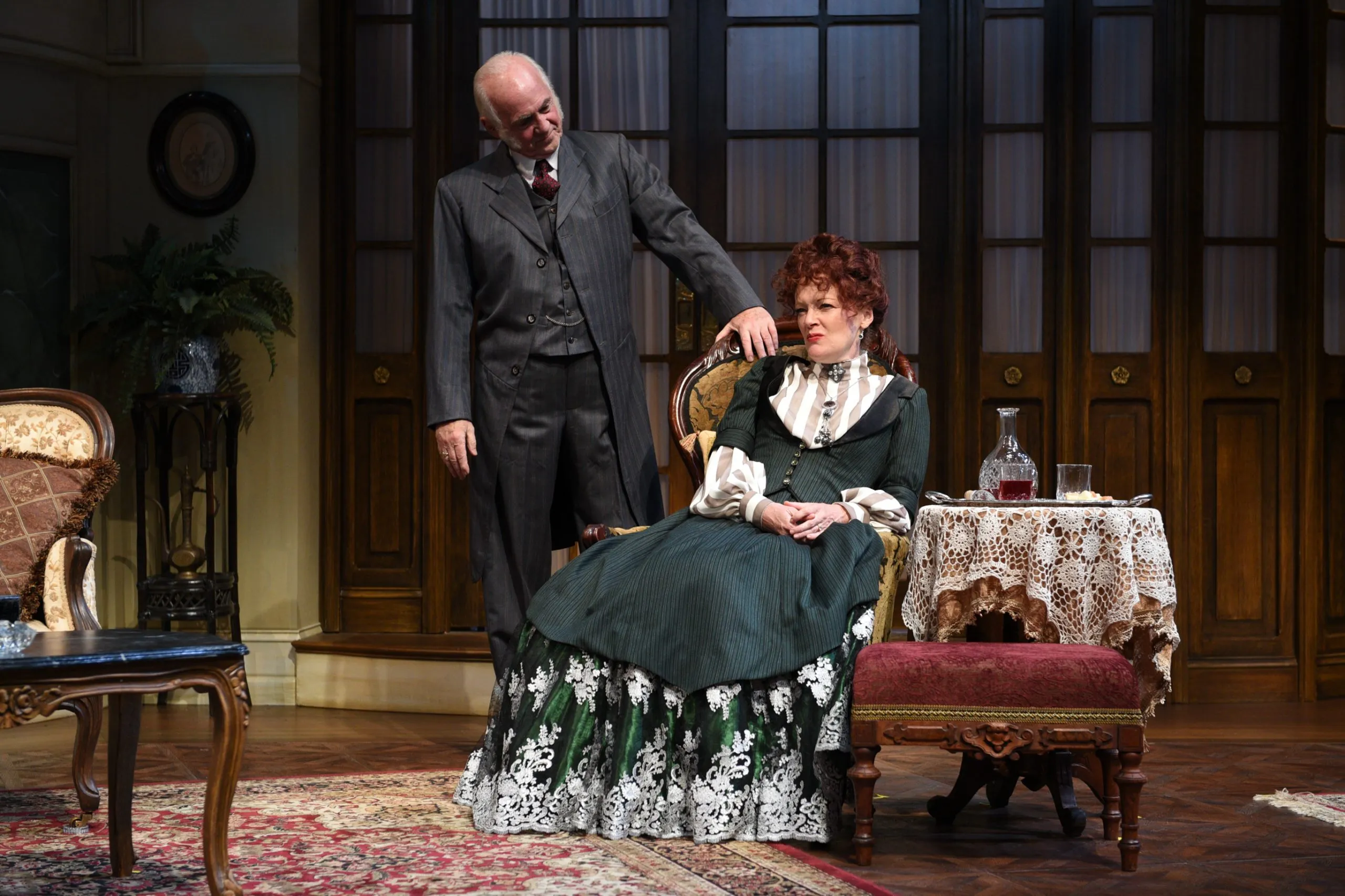 Man standing up while fixing the woman hair sitting on chair.
A man with glasses adjusting a woman's collar on a red dress.
